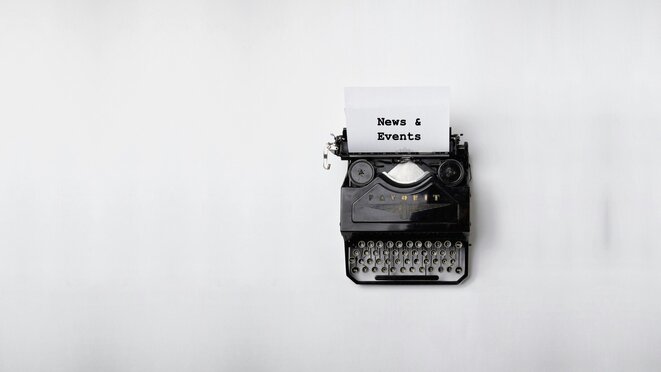 Old black typewriter on white background. News and Events is written on the paper in the typewriter.