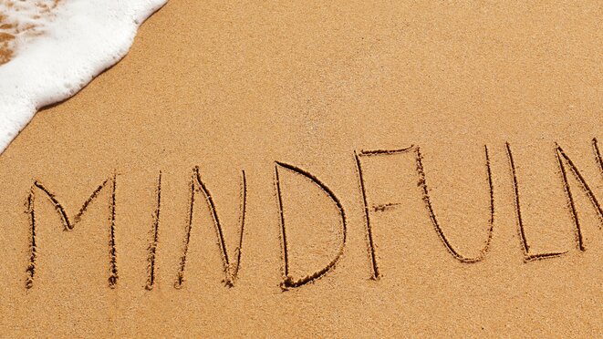 The word mindfulness written in the sand of a beach