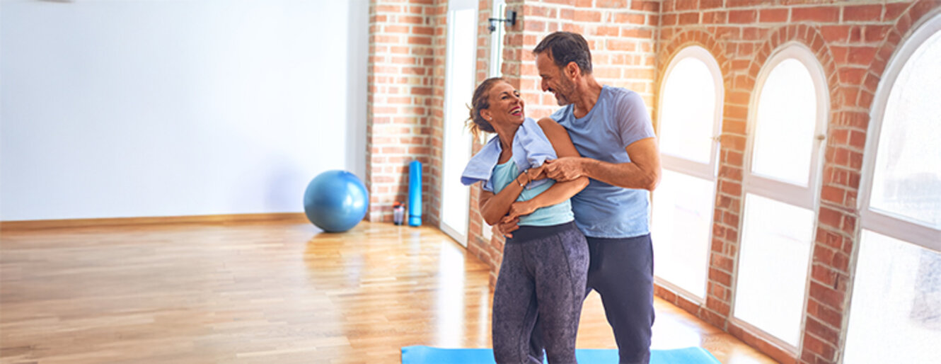 Middle age beautiful sporty couple smiling happy. Standing with smile on face hugging at gym